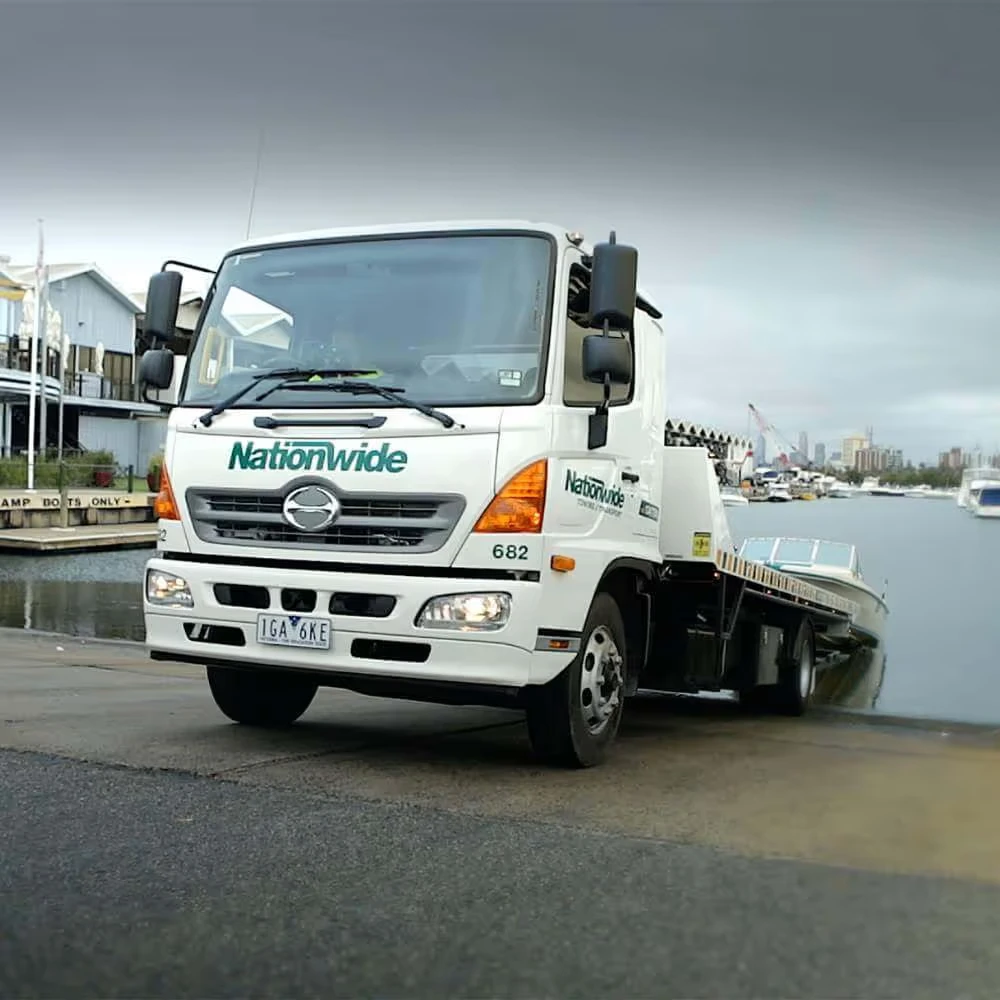 A tow truck is backing a boat into the water at a boat ramp.