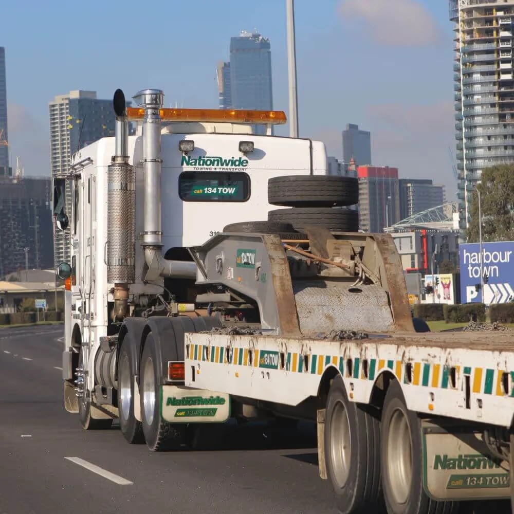 White Nationwide towing truck driving on a city road with high-rise buildings in the background.