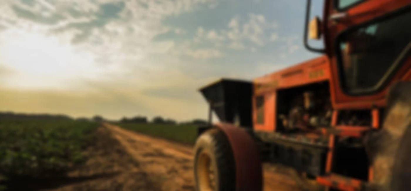 A red tractor sits idle on a dirt path next to a green field.