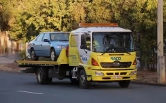 A tow truck transports a blue car on a city street during the day.