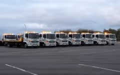 A line of eight white tow trucks with yellow lights parked on a paved area.