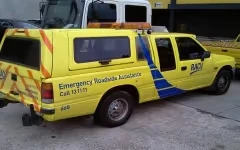 Yellow emergency roadside assistance pickup truck with blue and red markings parked on concrete.