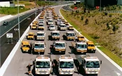 Multiple orange and white trucks lined up in several rows on a wide paved road.