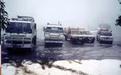 Four off-road vehicles parked on a muddy surface in foggy weather.
