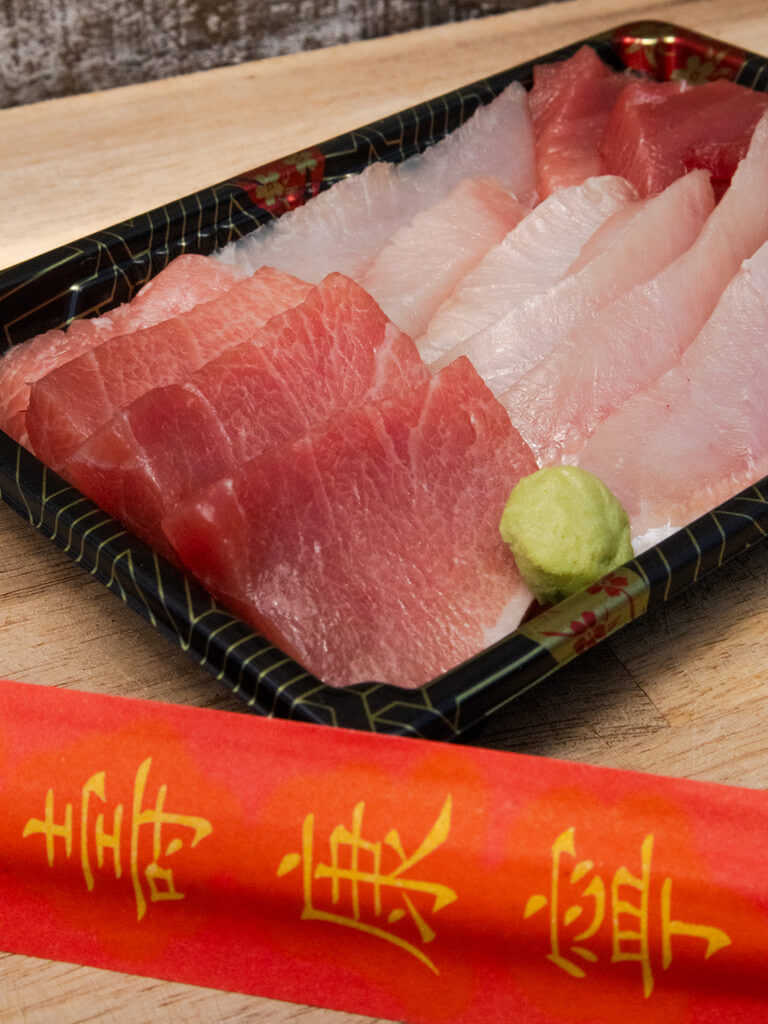 Close up of sashimi tray on wooden cutting board with chopsticks in foreground