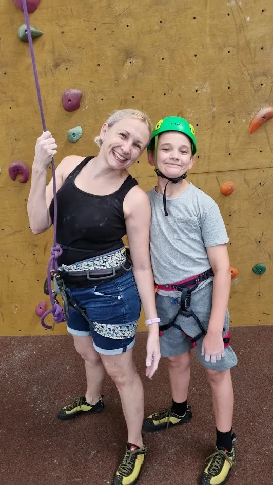 A woman and a young boy smiling in indoor rock climbing equipment