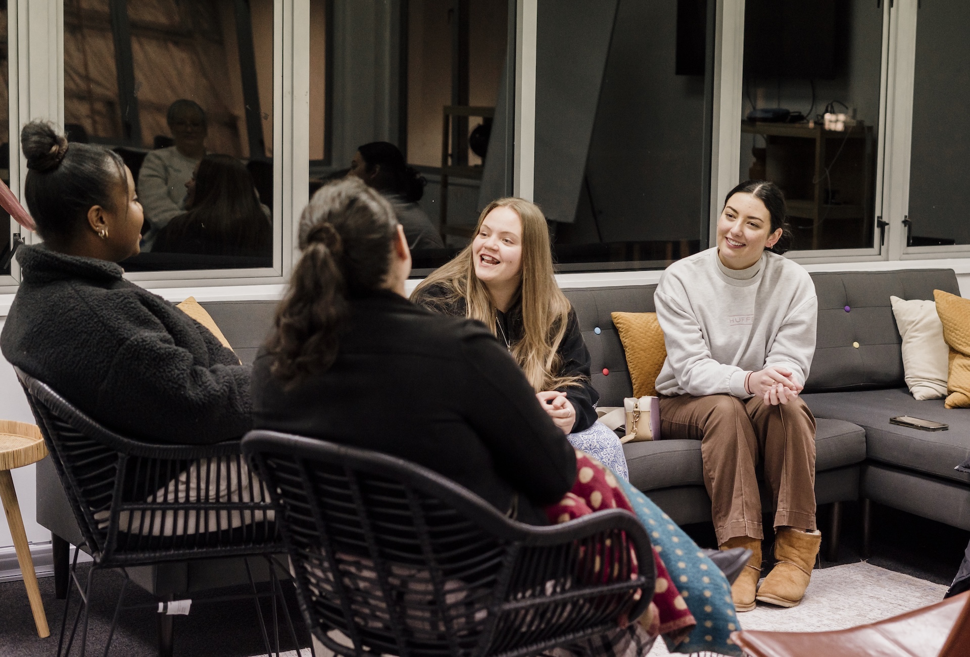 Two women in safety vests smiling outside an industrial building with cars parked nearby.