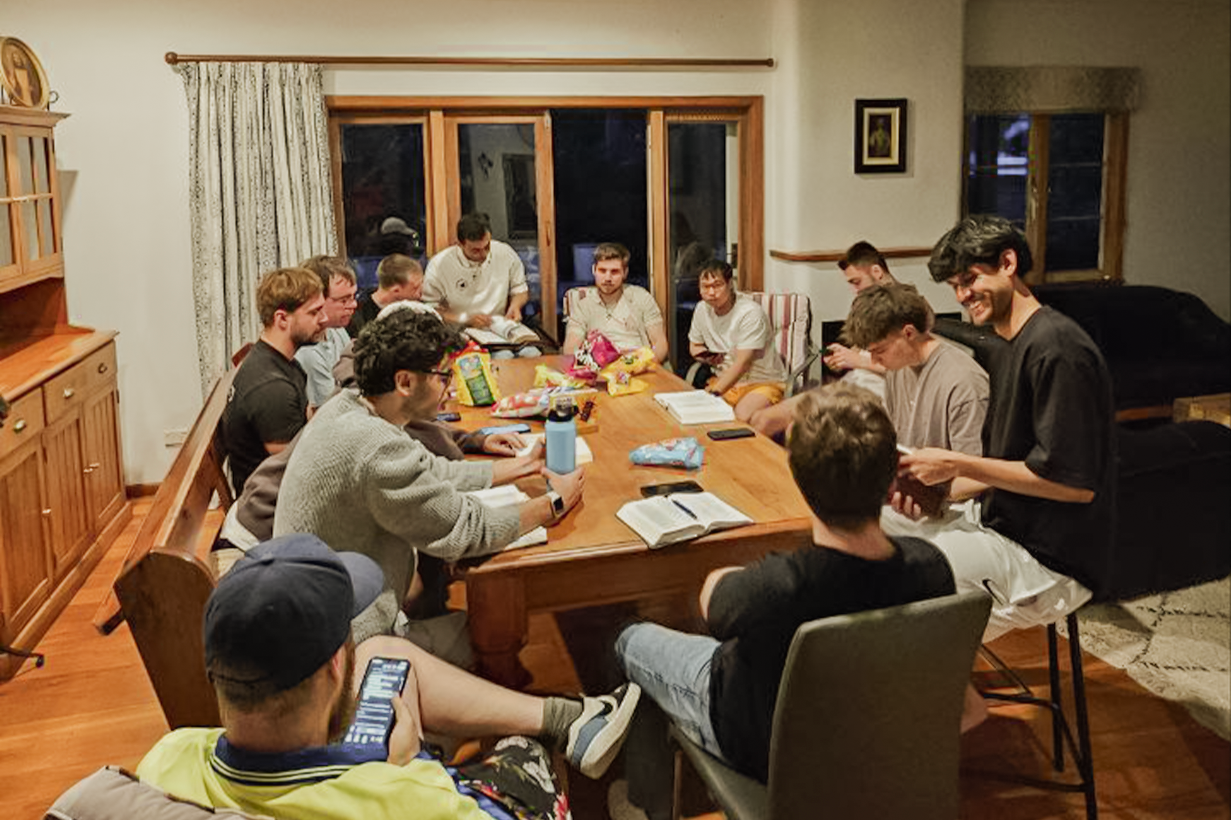 Two women in safety vests smiling outside an industrial building with cars parked nearby.