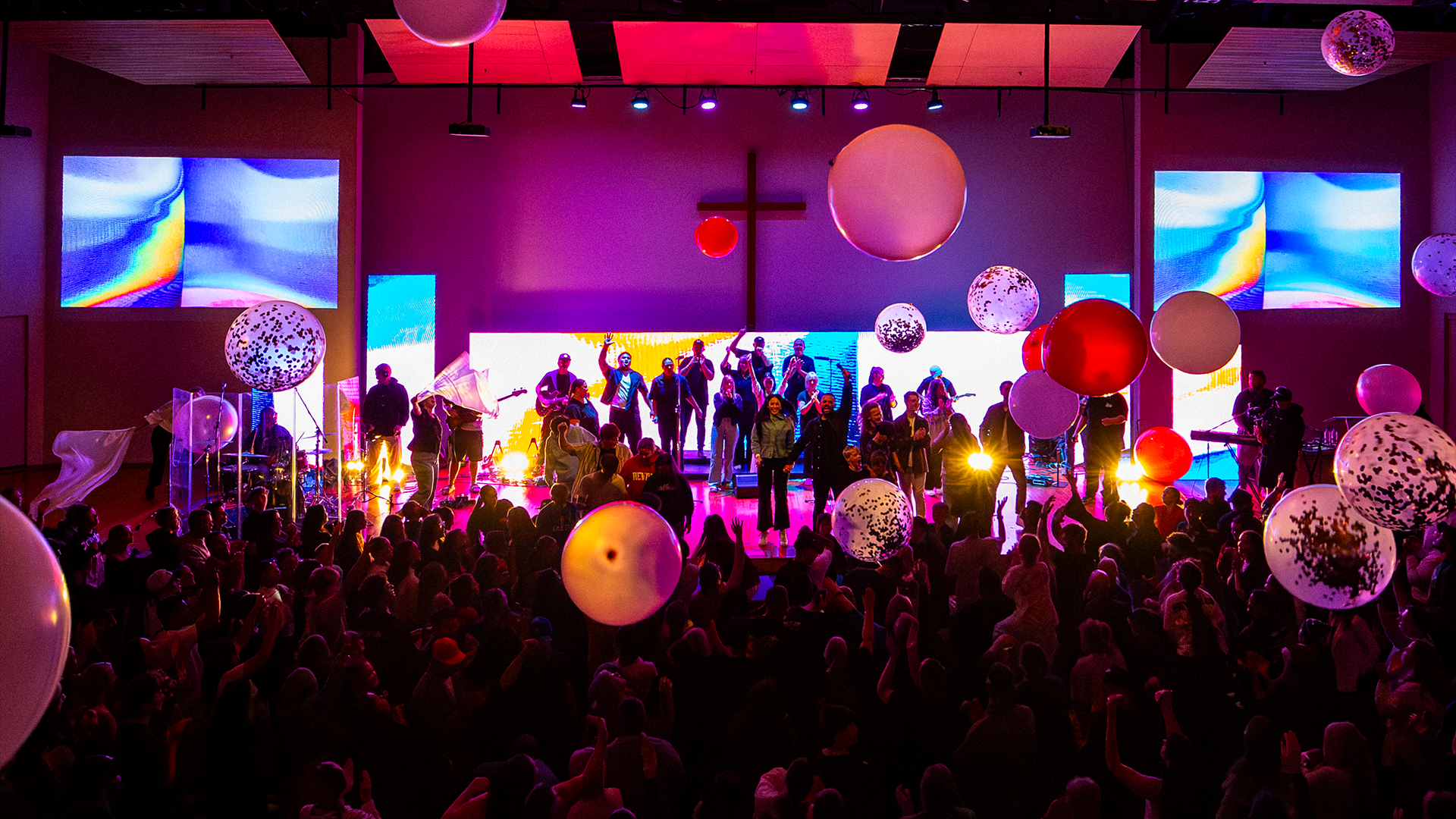 Crowd celebrating indoors with raised hands and joyful expressions.