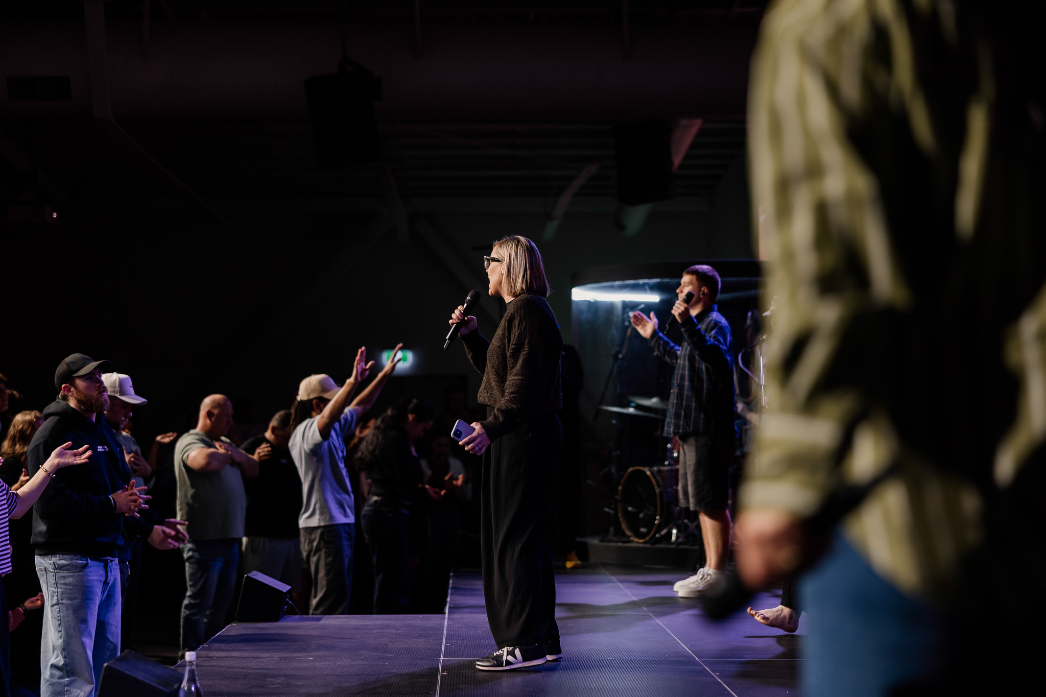 People raising hands in a worship service or concert atmosphere.