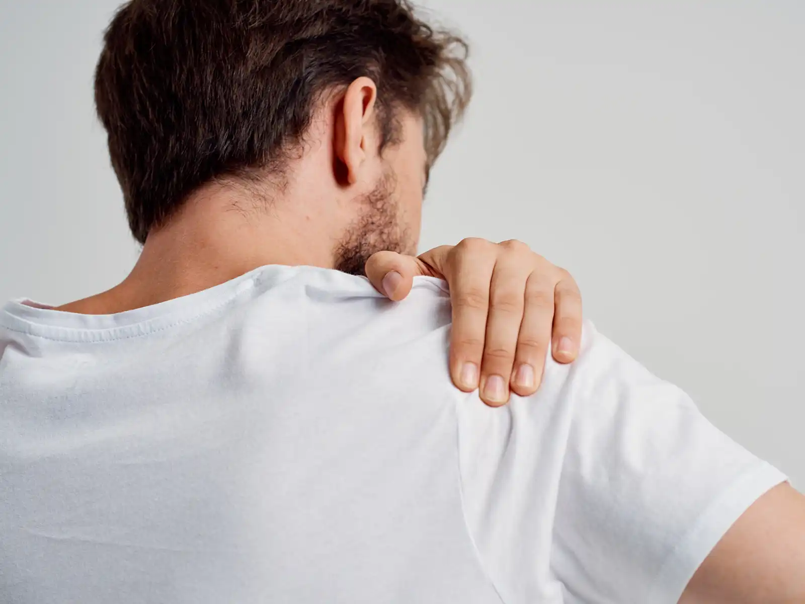 A man in a white t - shirt holding his neck