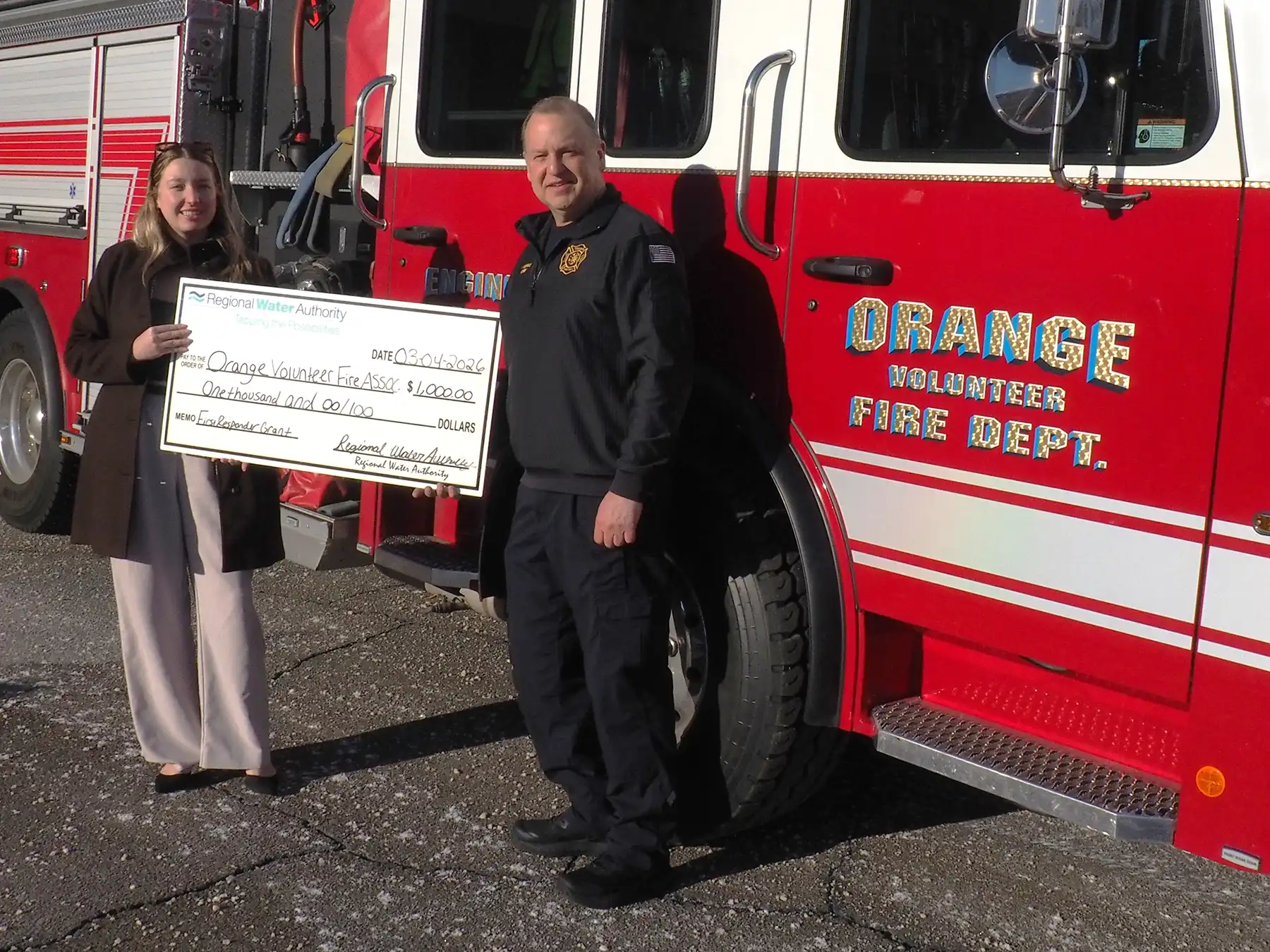 Nicoletta Blevins presents a $1,000 Regional Water Authority check to Orange Volunteer Fire Dept. Chief Vaughan Dumas in front of a fire truck.