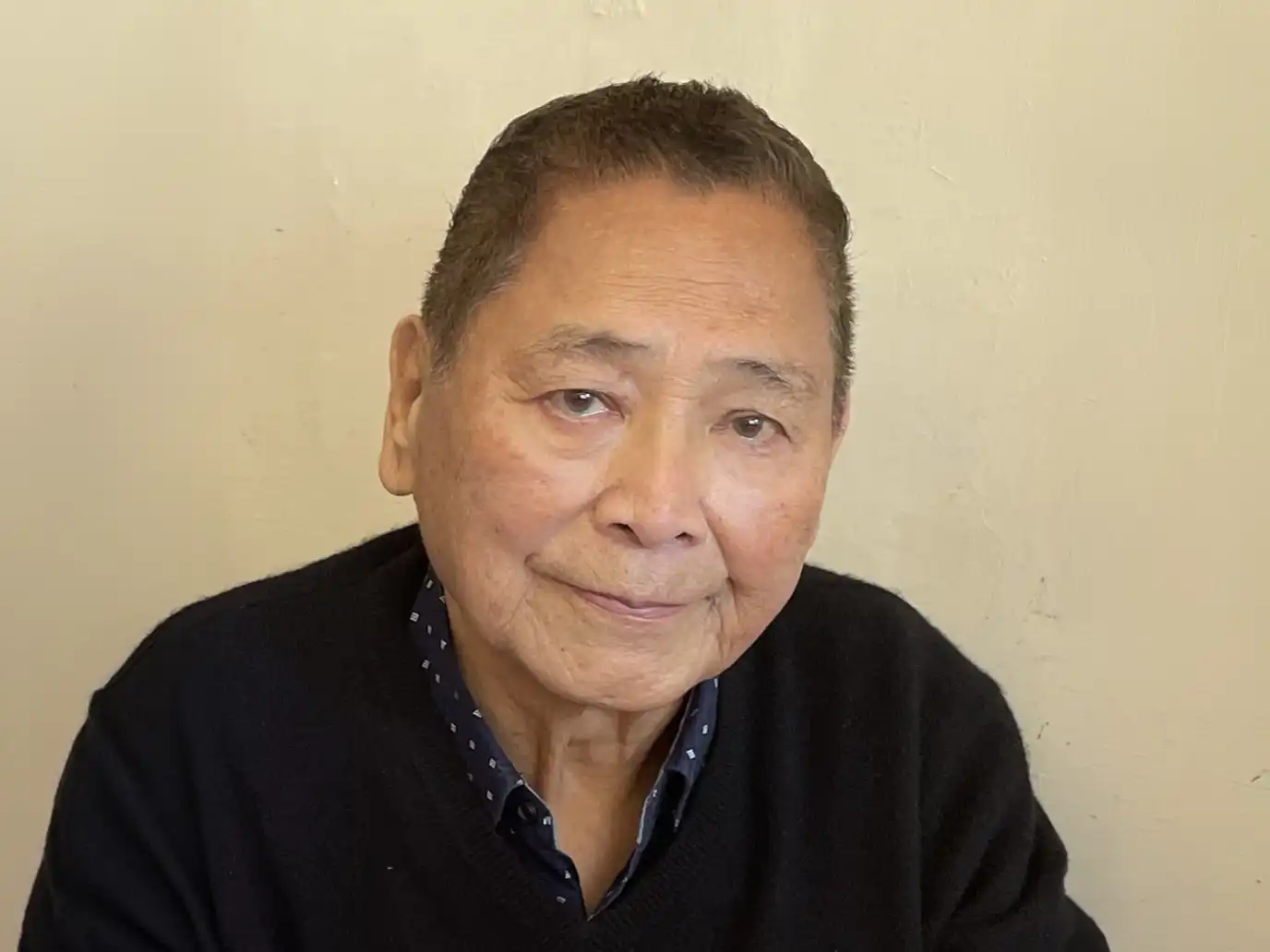 Portrait of Dr. Pang-Hsung Wang, an elderly Taiwanese man with a gentle smile, wearing a black v-neck sweater over a patterned blue collared shirt.