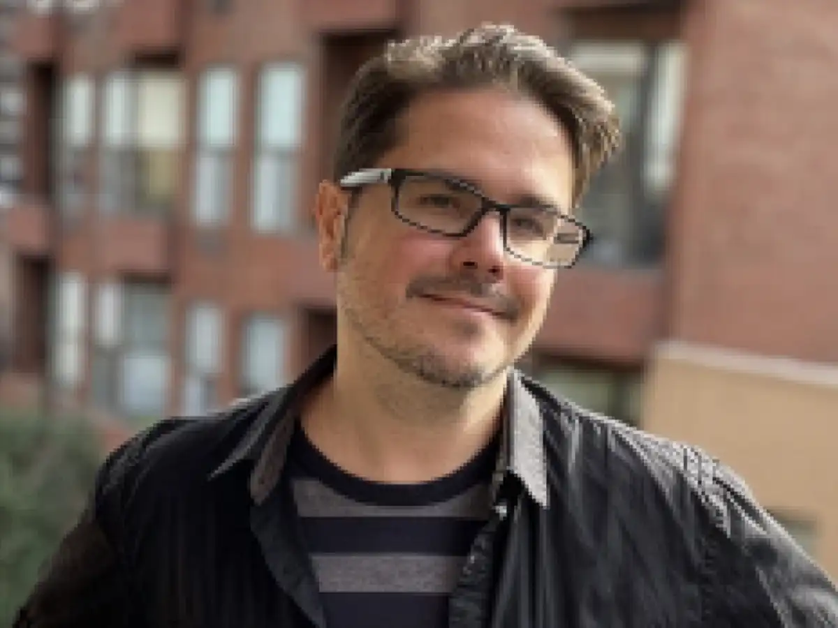 Author and graphic novelist Dave Roman wearing glasses and a striped shirt, smiling in a professional headshot for his upcoming Amity school workshop.
