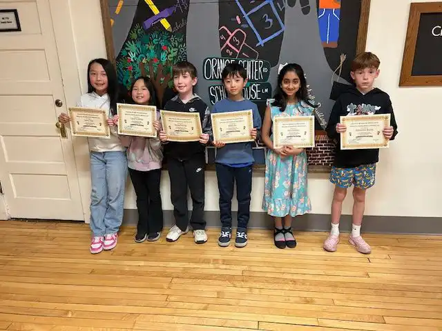 Six elementary students proudly display their achievement certificates while standing in a line at the district spelling bee held at the Board of Education.