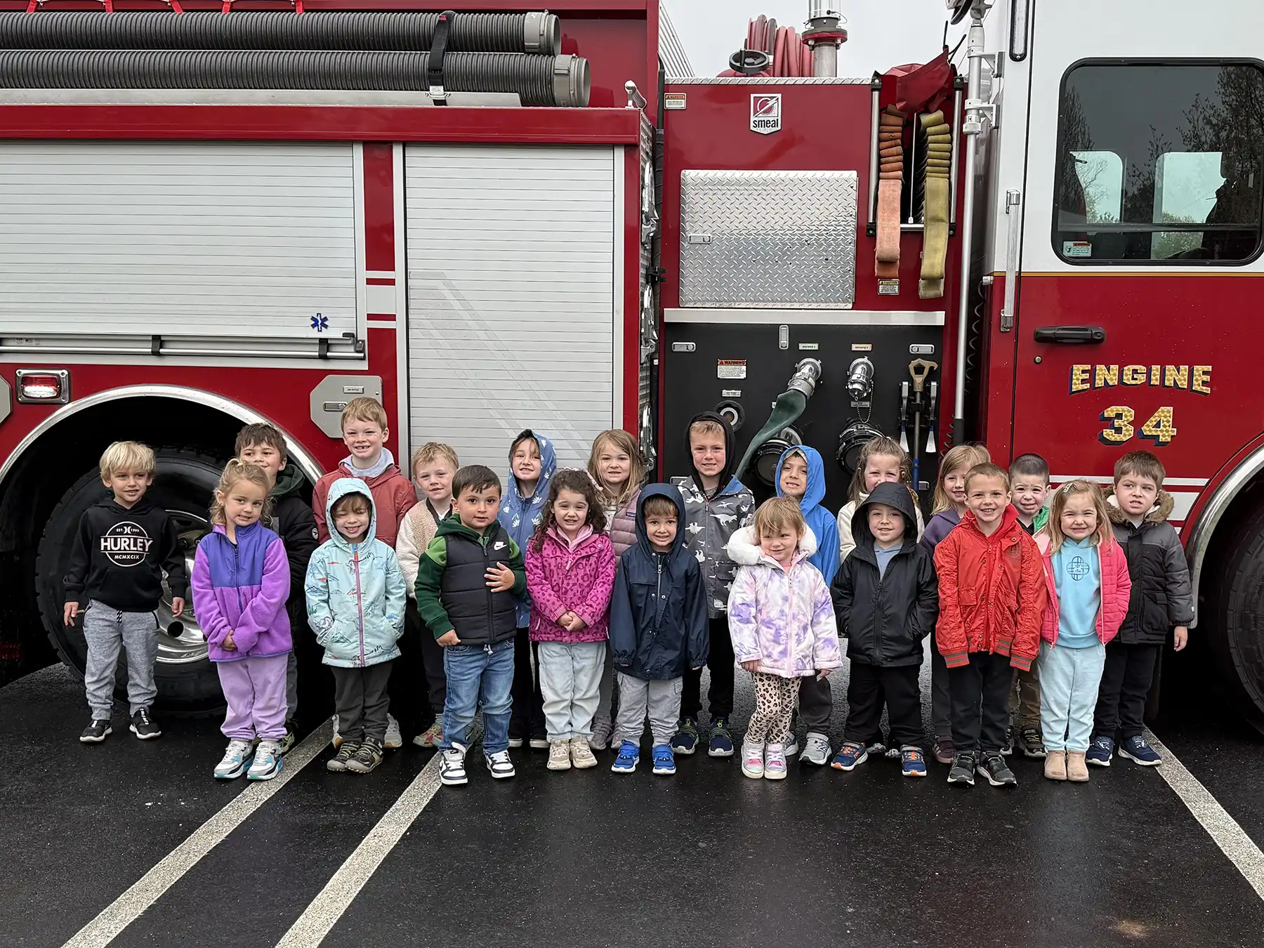A group of nursery school students in colorful jackets pose in front of a red OVF Engine 34 fire truck during a fire safety education visit in Orange.