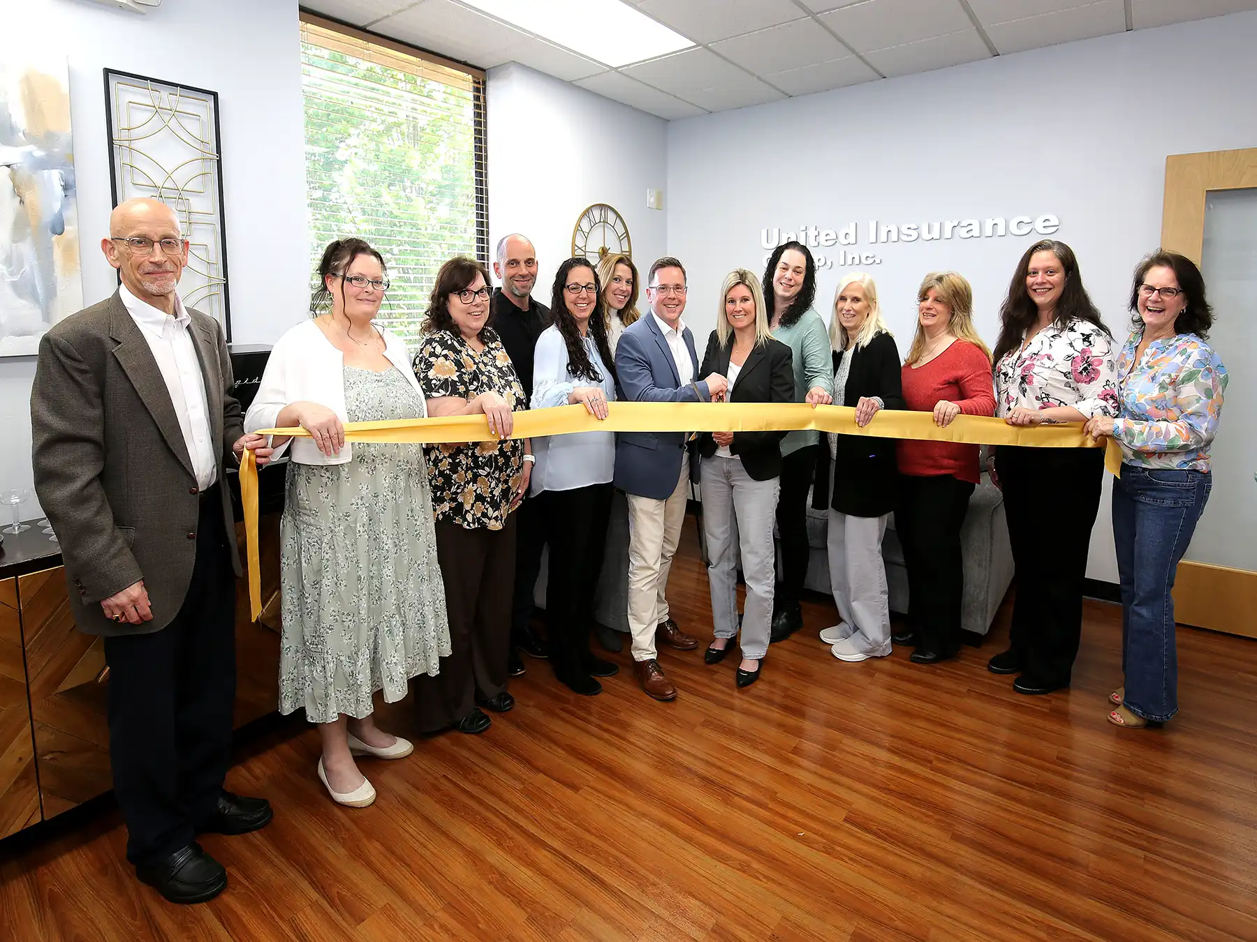 A diverse group of staff and local dignitaries participate in a formal yellow ribbon cutting ceremony to celebrate the opening of United Insurance Group, Inc.