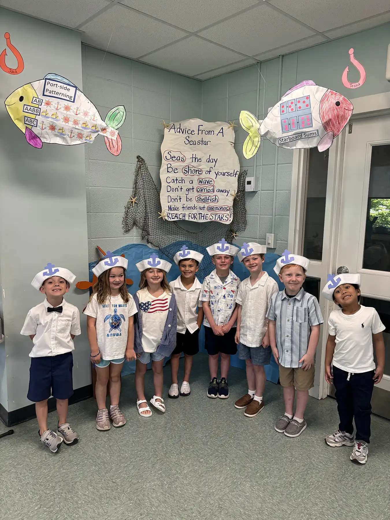Young students wearing sailor hats pose in a classroom decorated with fish and ocean crafts at Orange Community Nursery School.