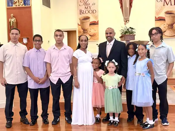 Drs. Rey and Dennie Ramos stand on the right, with the mother visibly pregnant, happily surrounded by their eight children ranging in age from young kids to teenagers