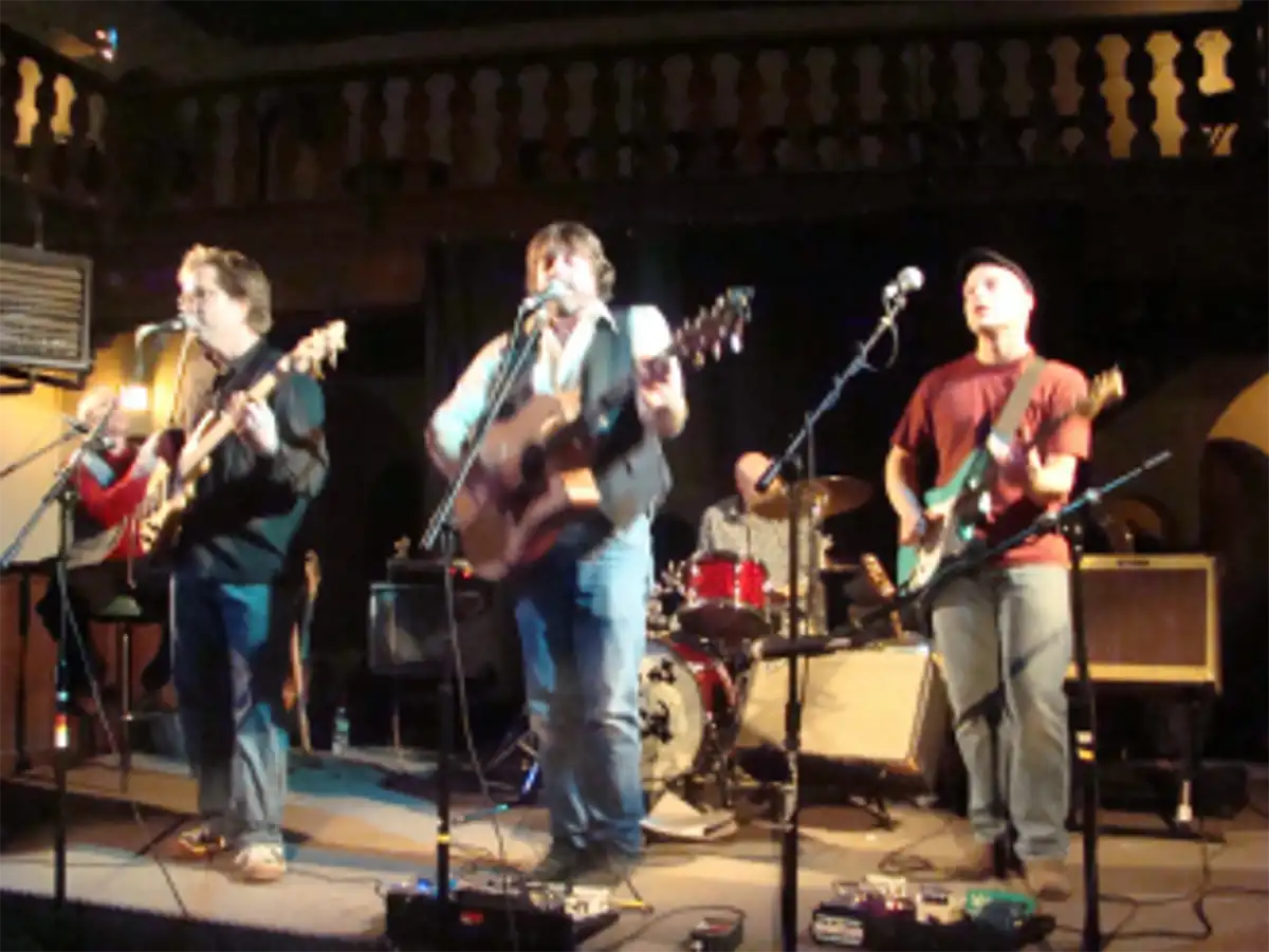 John Mayock and the Homesteaders performing live on a dimly lit indoor stage.