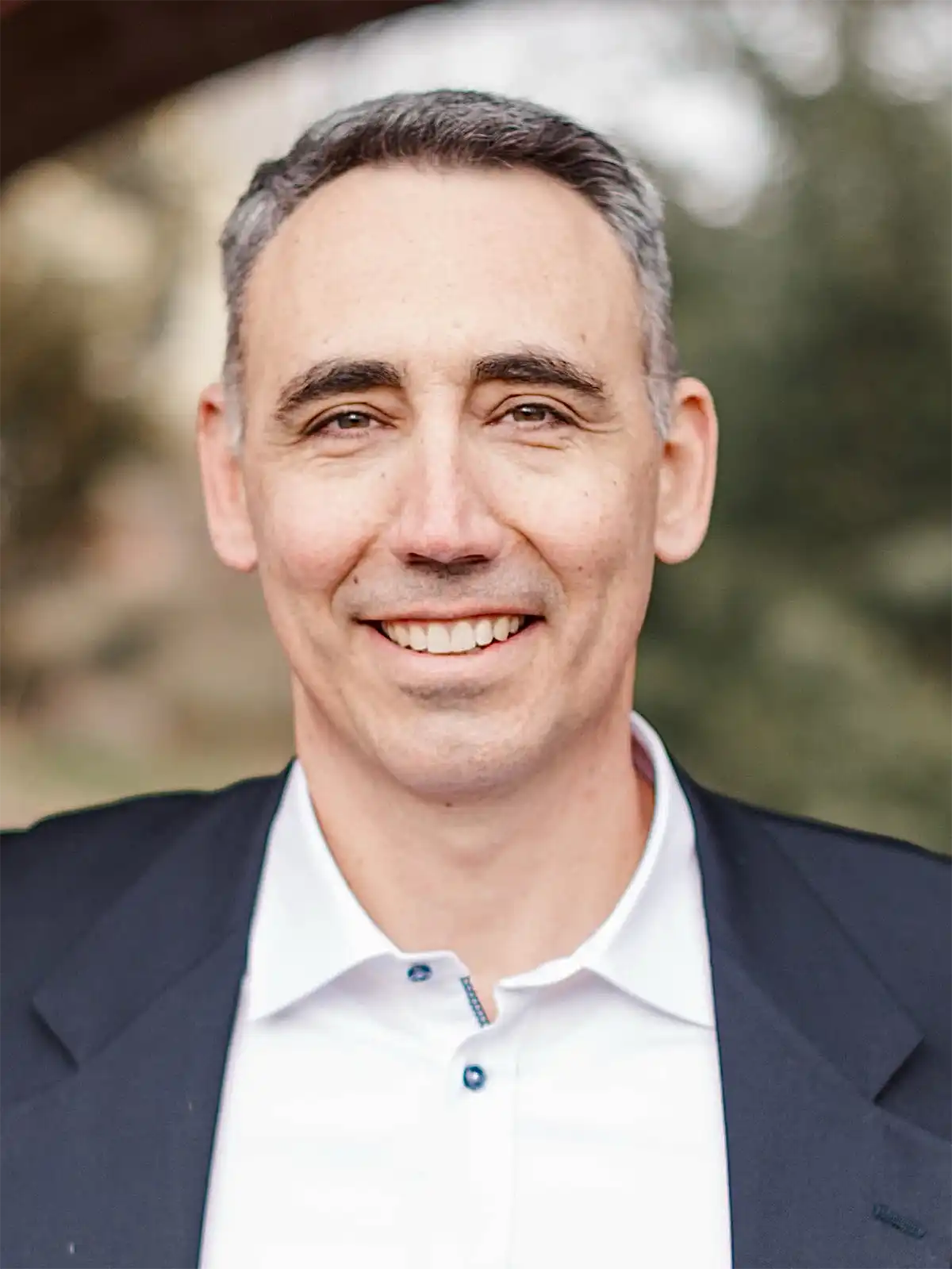 Professional portrait of Eric Lopez, CEO of Arrowhead Leadership Consulting, smiling outdoors in a dark suit jacket and white collared shirt.