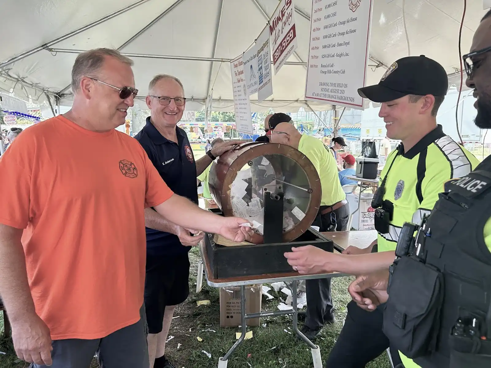 Firefighters and police officers pull a winning raffle ticket from a wooden drum under a tent during the Orange Volunteer Fire Department carnival.