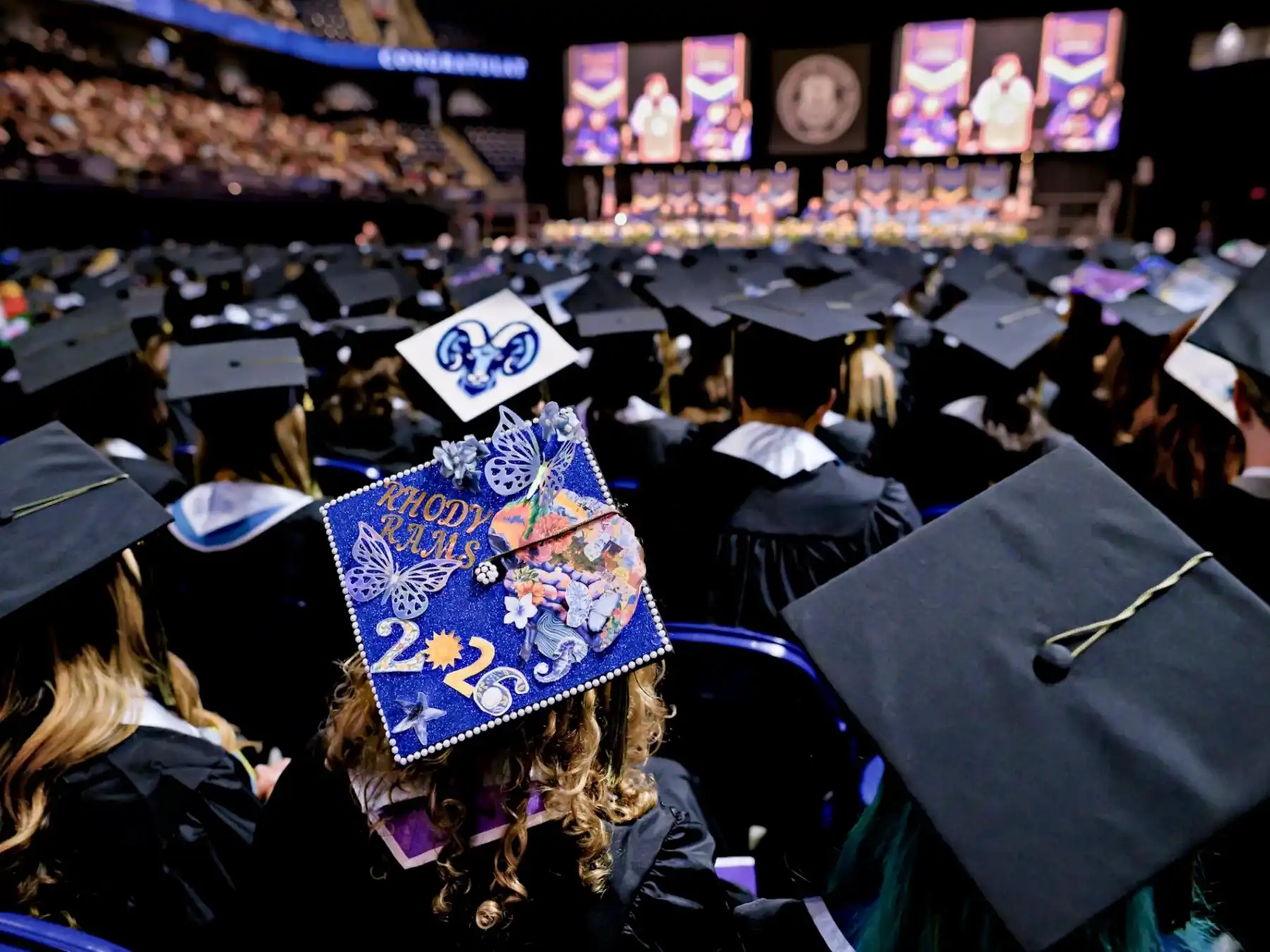 University of Rhode Island graduates in caps and gowns sit in an arena facing the stage during the 2026 commencement ceremony.
