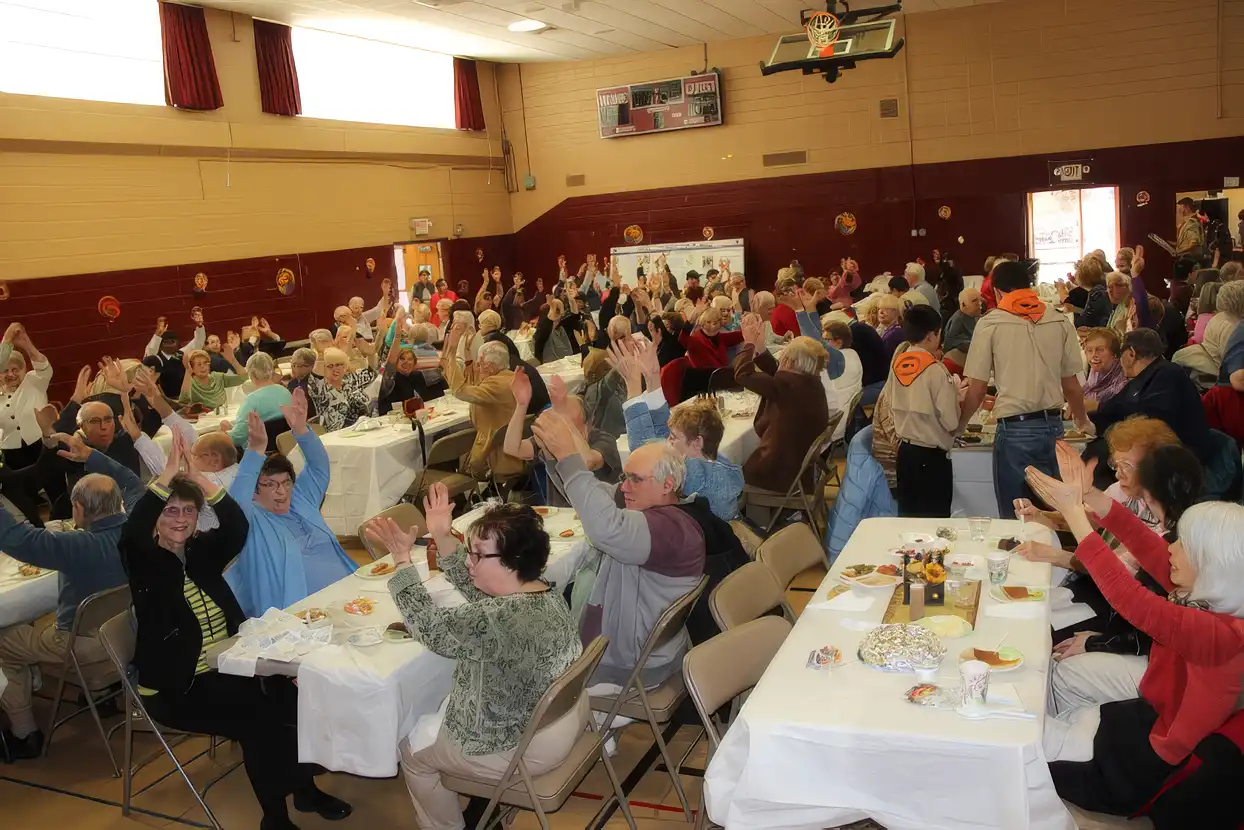Guests wave and celebrate at long dining tables during the annual Orange Lions Club Thanksgiving dinner at High Plains Community Center.
