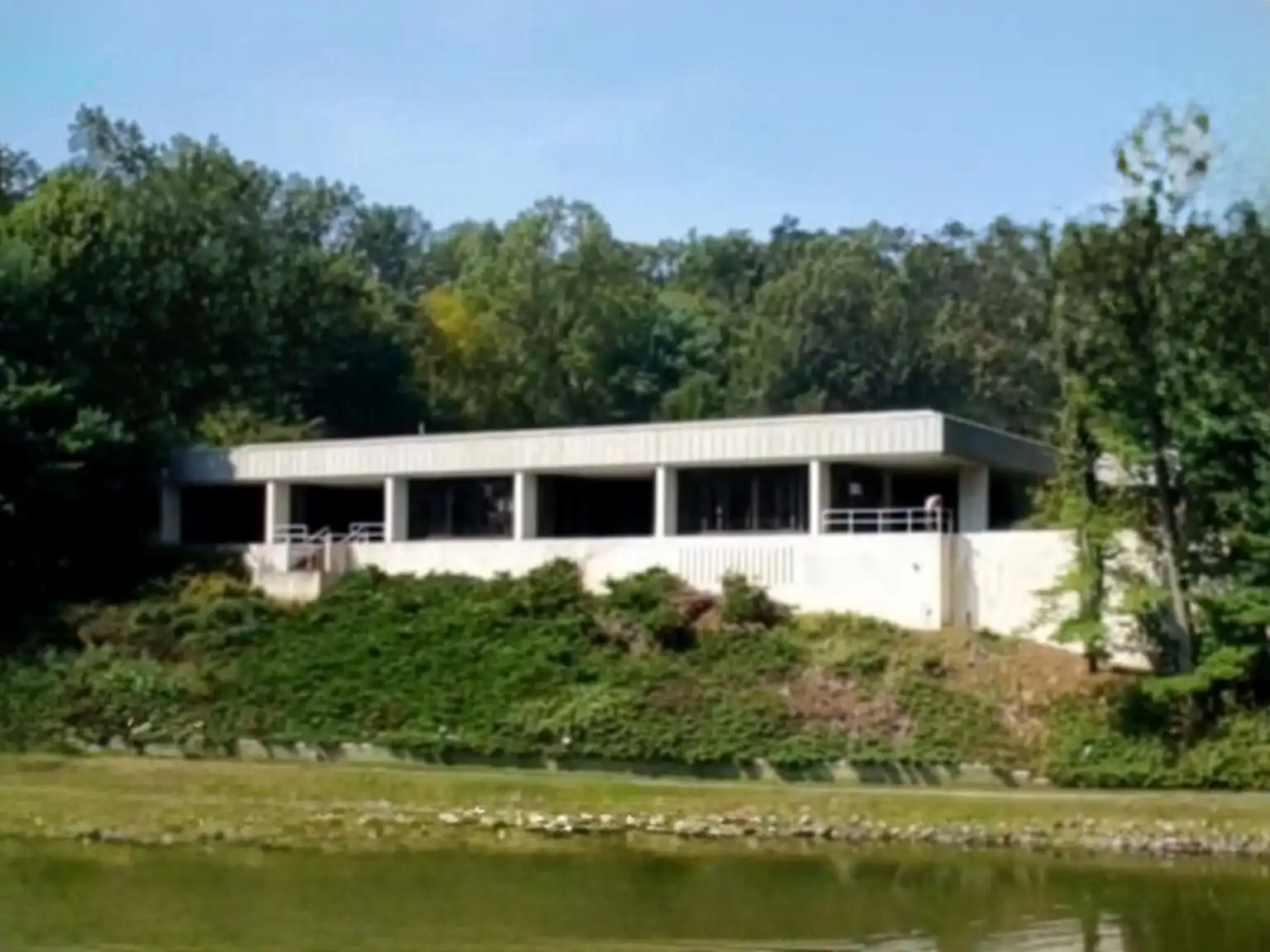 Exterior view of the former University of New Haven building on Derby Milford Road in Orange, situated on a grassy hill overlooking a pond.