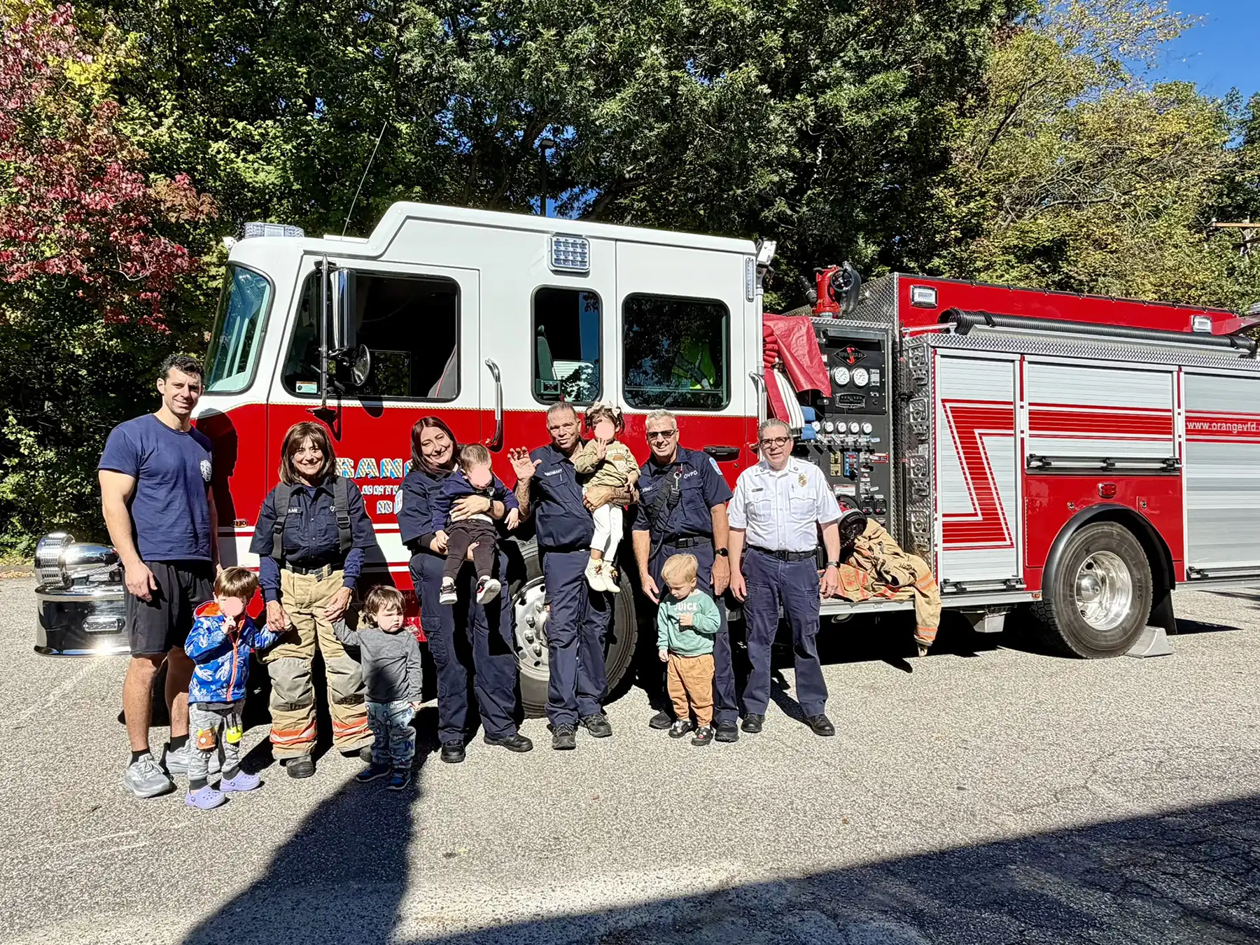Orange Volunteer Fire Department firefighters and staff posing outdoors in front of a red and white fire engine with young preschool children.