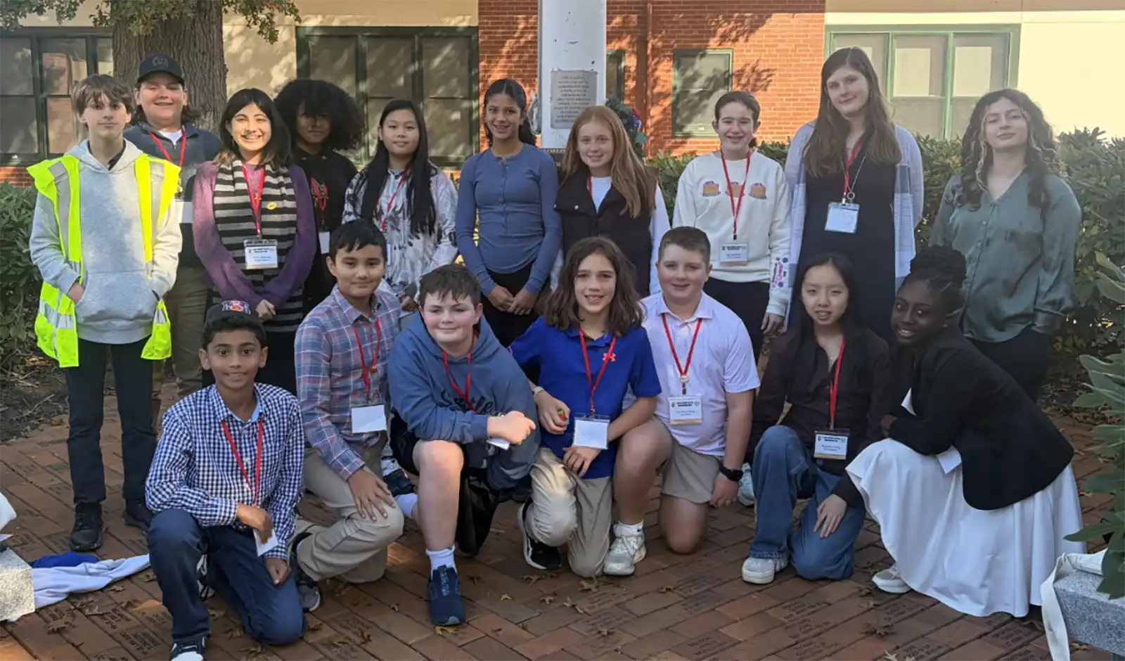 Seventeen Amity Middle School students wearing name badges gather outdoors during Orange Government Day after shadowing local municipal leaders.