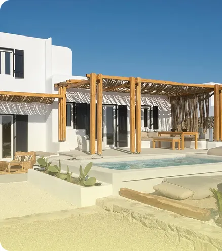 Modern white villa with wooden pergola, outdoor seating, small pool, and desert landscaping under a clear blue sky.