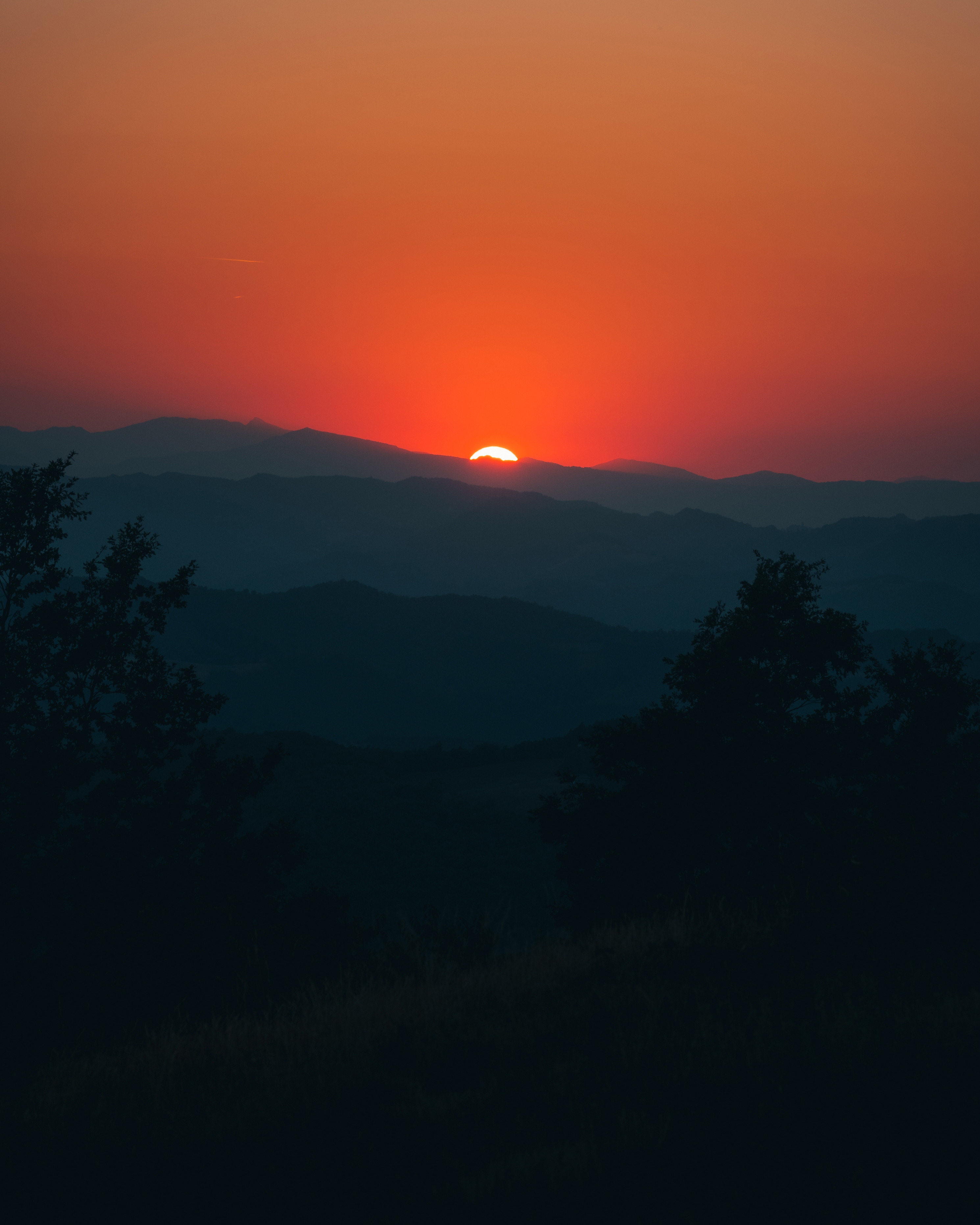 Photo of sun setting in the background over a layer of mountain ranges in the Italian countryside