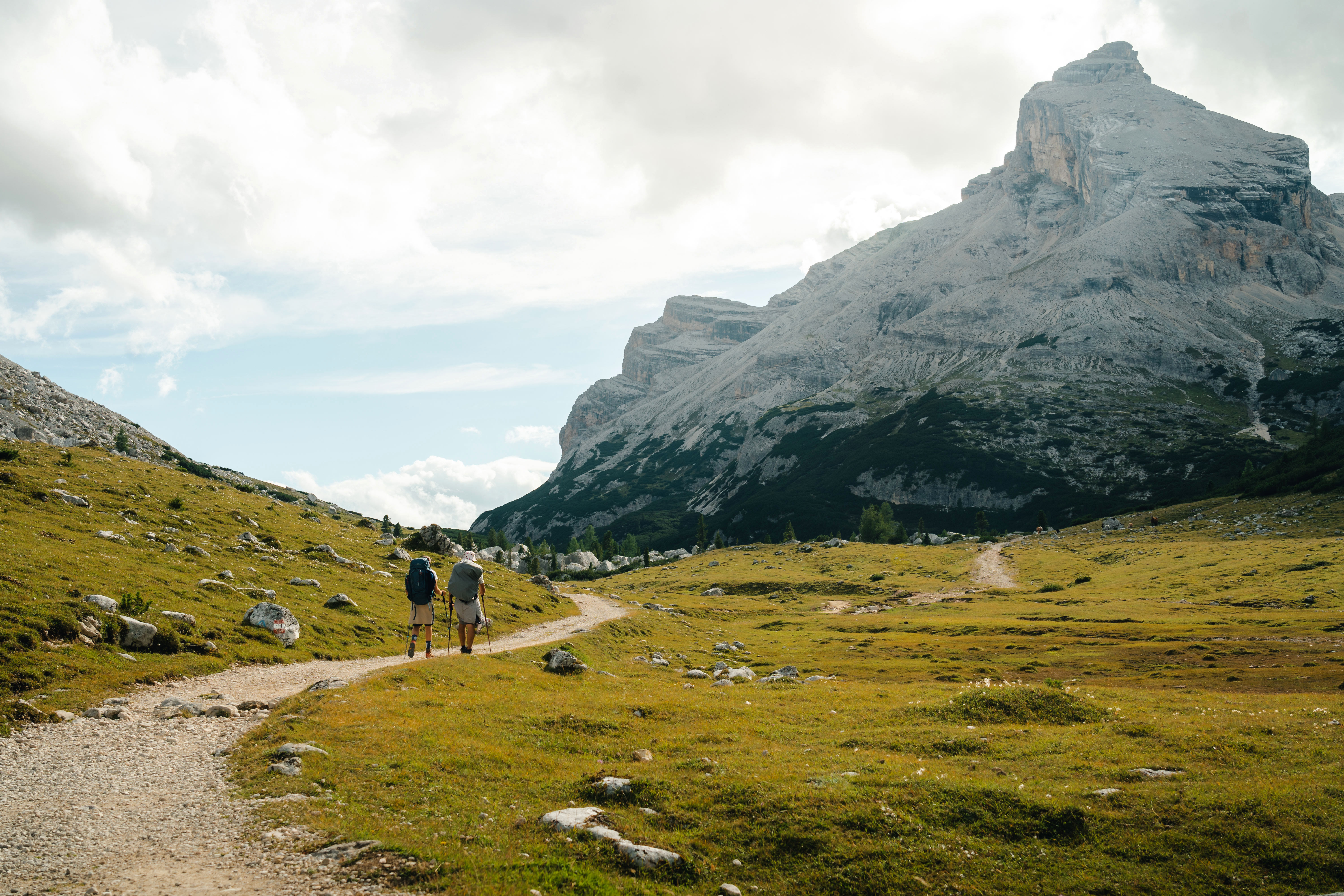 Photo of two hikers walking along a trail, with a mountain towering in the background
