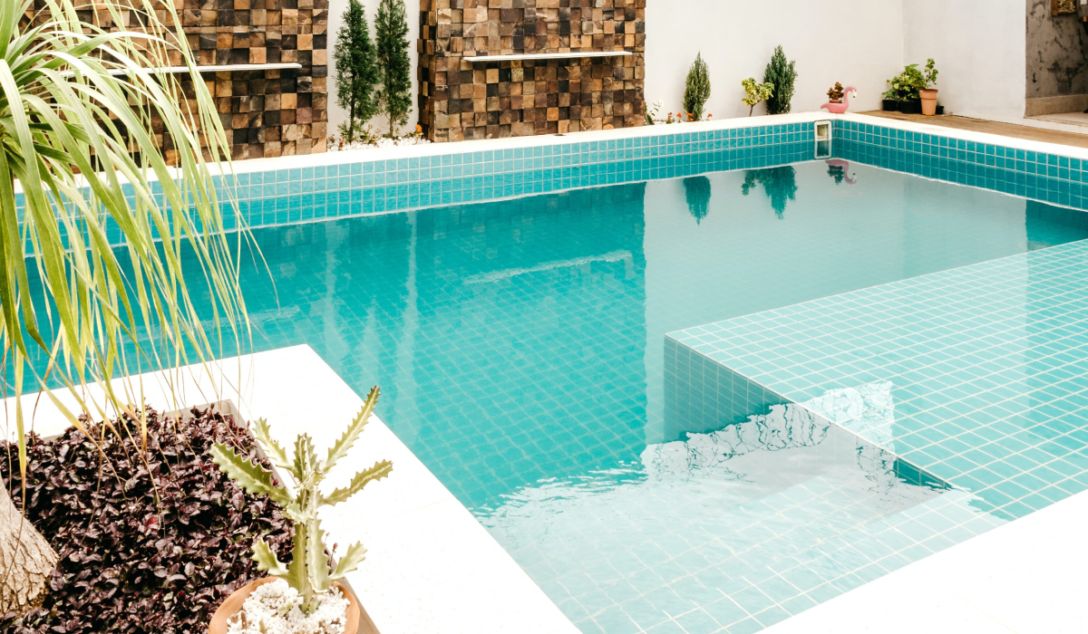 Backyard pool with blue mosaic tile and a raised sun shelf surrounded by potted plants