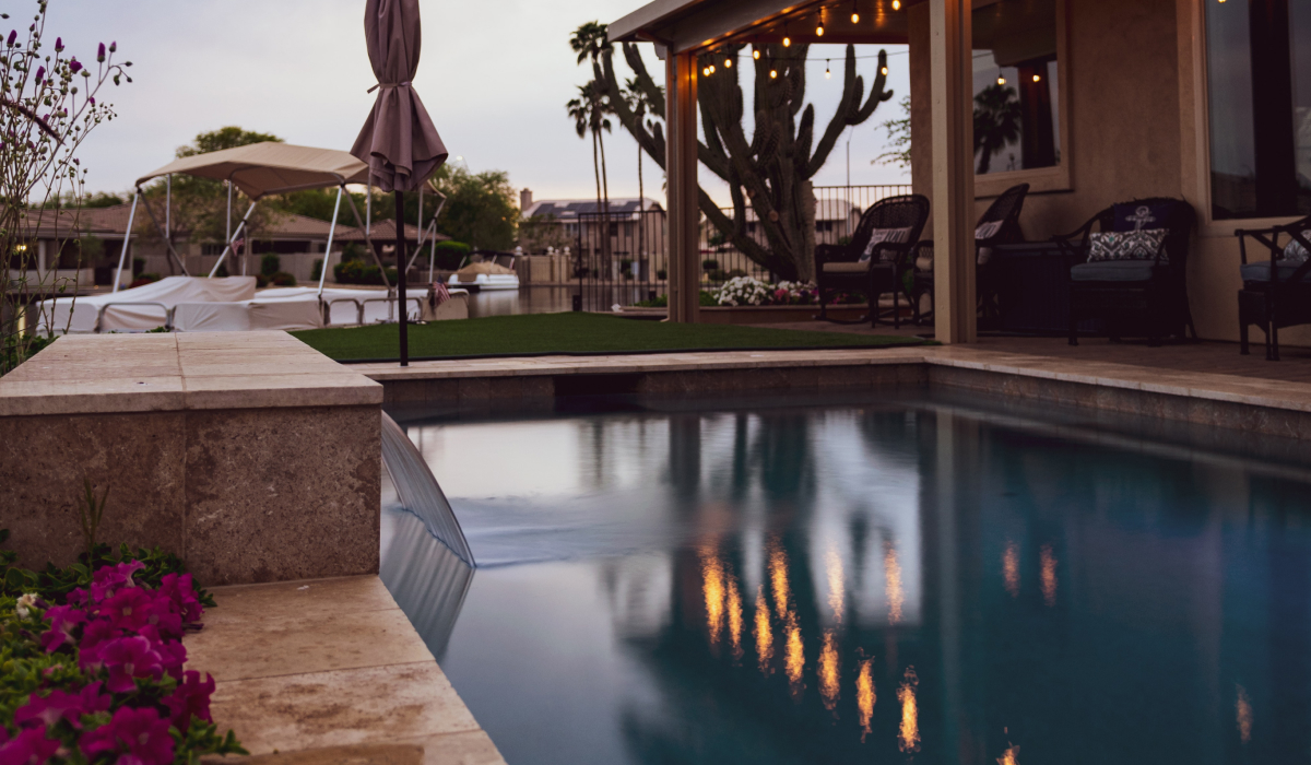 Pool with a stone waterfall feature and covered patio lit with string lights at dusk