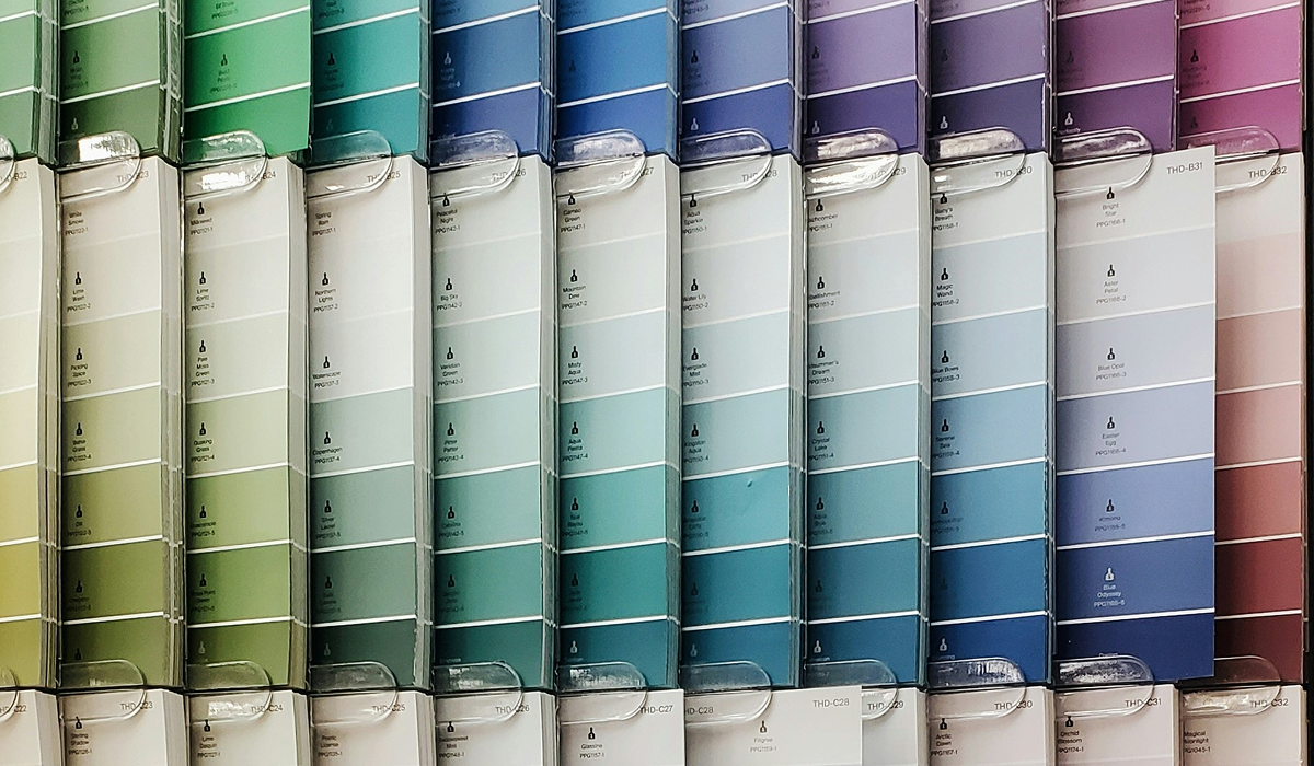Rows of Behr paint sample cards in a home improvement store display, arranged in a gradient from greens and teals through blues to purples and pinks.