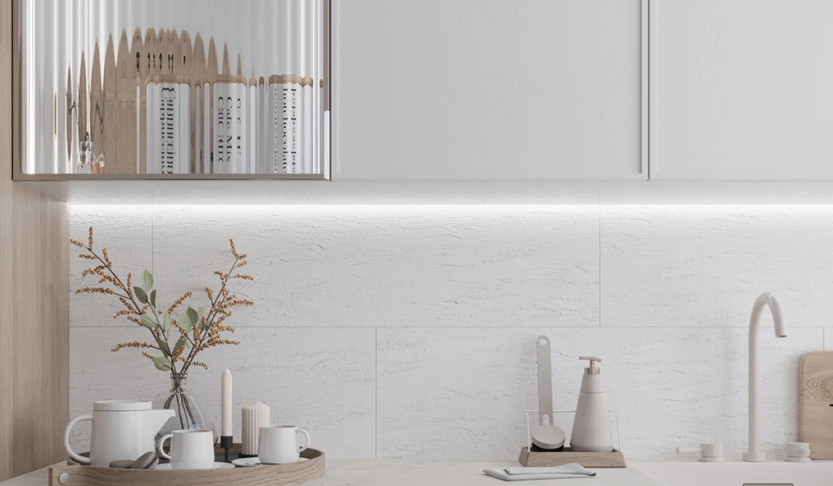 All-white kitchen with a textured stone-look backsplash, under-cabinet LED lighting, and a fluted glass cabinet reflecting the room.