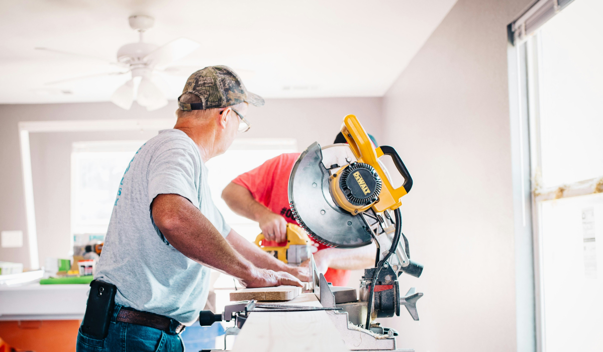 Two construction workers using a DeWalt miter saw to cut trim inside a partially finished home.