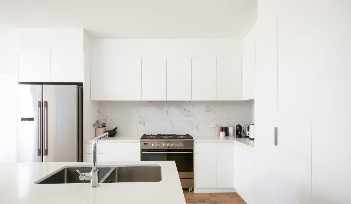 All-white minimalist kitchen with marble slab backsplash, stainless appliances, and a white waterfall island