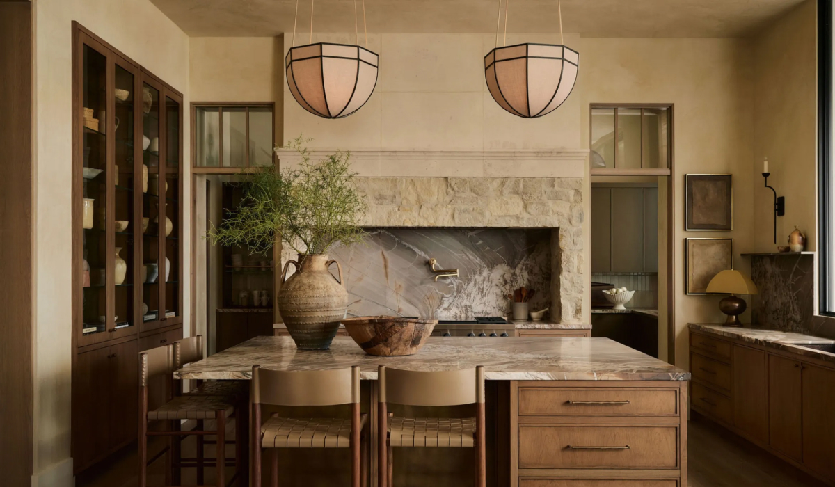 Warm neutral kitchen with wood island, stone-clad range hood, and dome pendant lights over a marble dining table