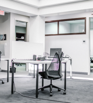 Modern office workspace with a white desk, black mesh chair, computer monitor, and office supplies on a gray carpet.