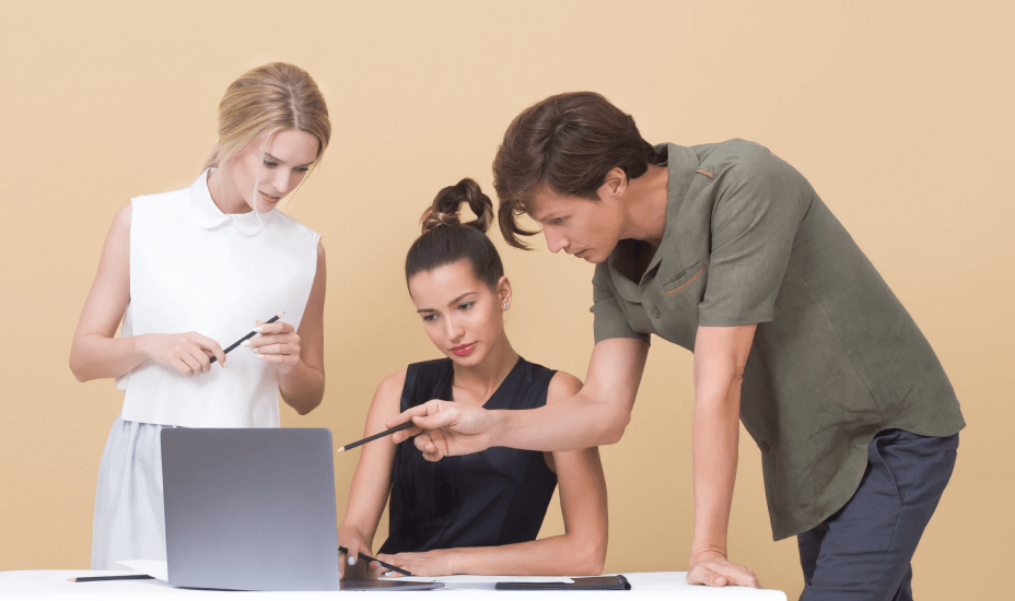 Three young professionals collaborating around a laptop, discussing and pointing at the screen.