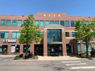 Brick commercial building with trees in front, housing 1st Bank and other businesses.