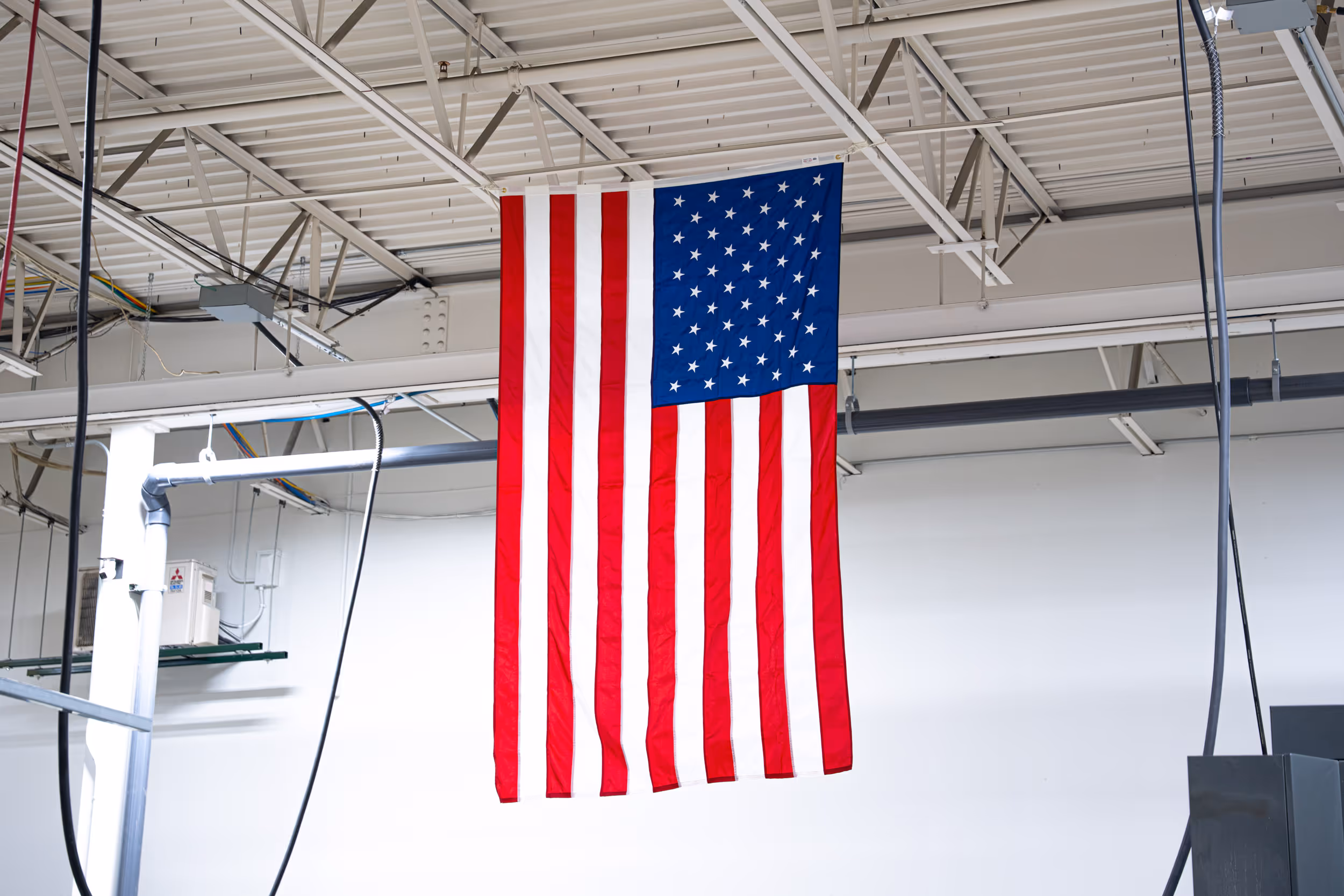 American flag hanging indoors from ceiling beams in 1Micro's warehouse.