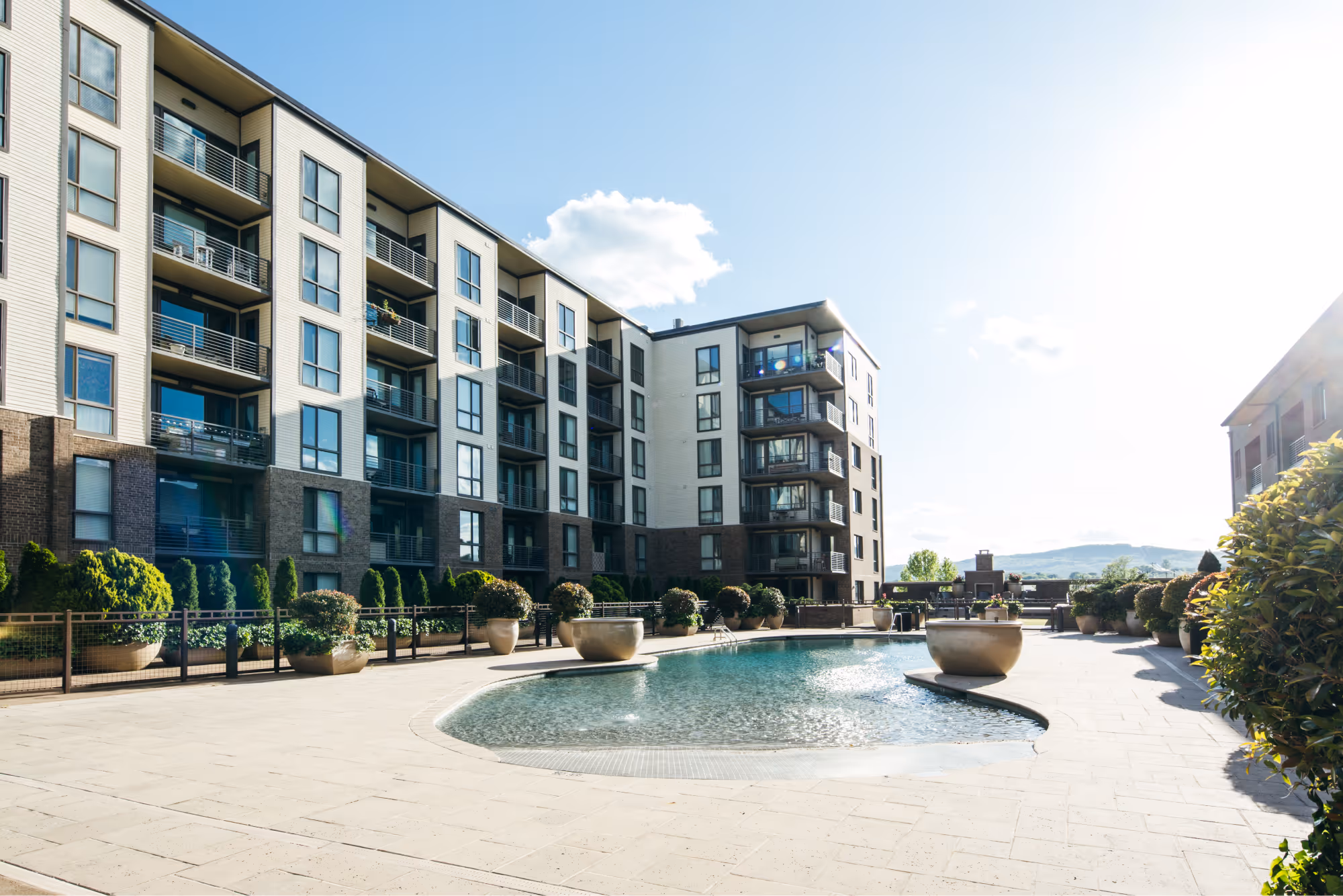Modern apartment complex with balconies surrounding a kidney-shaped outdoor swimming pool under a clear sky.