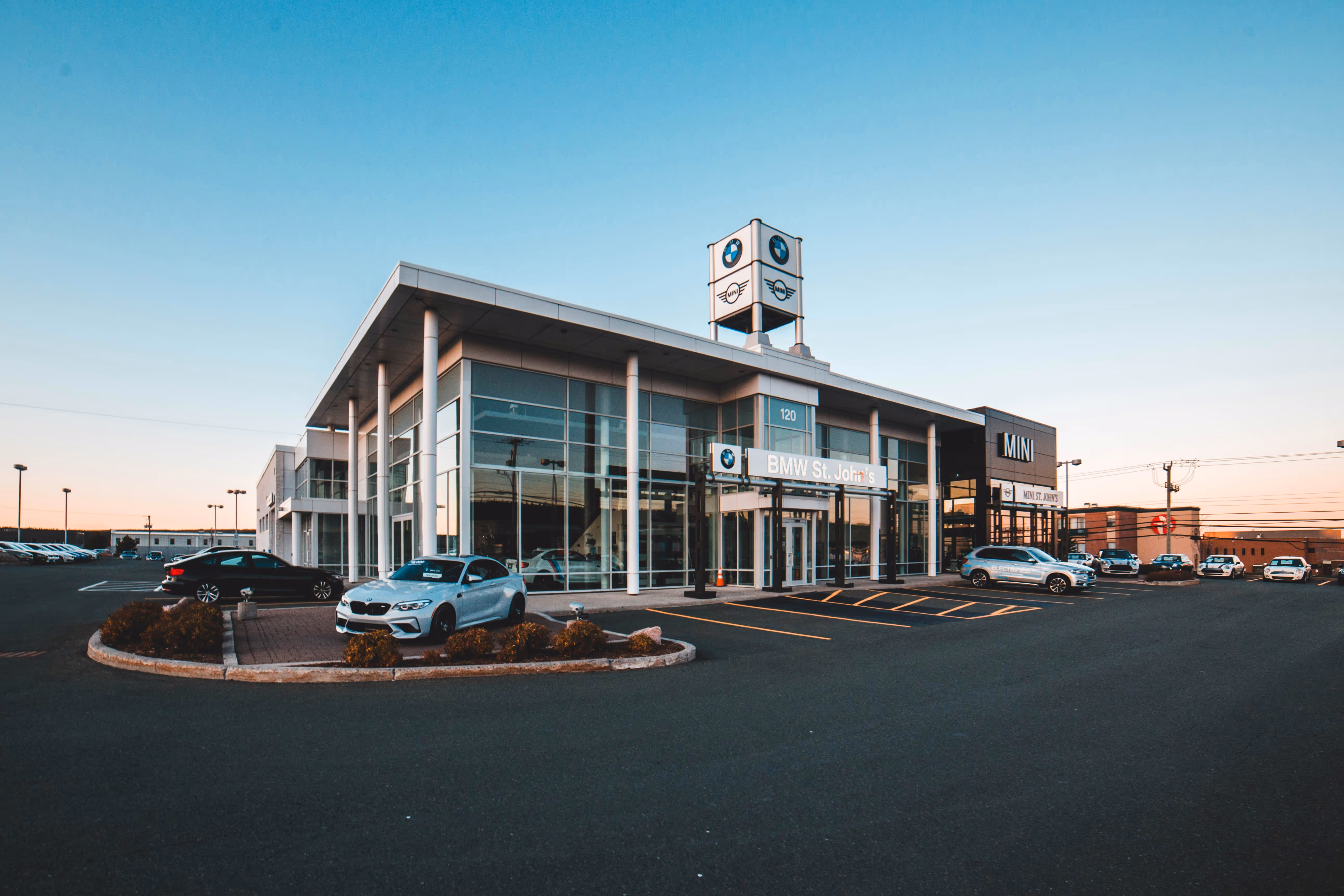 BMW St. John's and MINI dealership building with several parked cars under a clear sky at dusk.