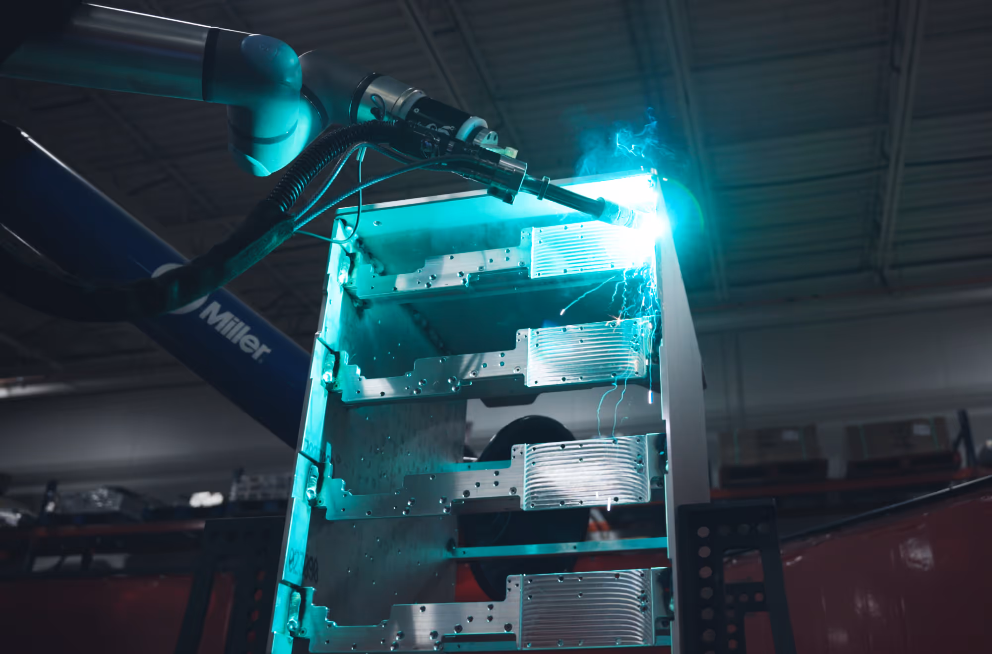 Robotic arm welding metal parts emitting bright blue sparks inside 1Micro's warehouse.