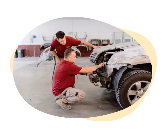 Two Sheen workers trying to fix the front of a wrecked vehicle. 