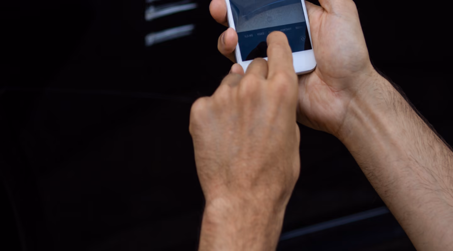 A man taking a photo of the front of his car with an iPhone.